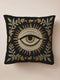 A black woven throw pillow with intricate gold and ivory embroidery featuring an Evil Eye motif, surrounded by botanical flourishes and sunburst details.